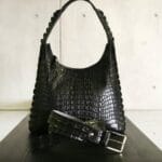 Czarna torebka z tłoczonej skóry i dopasowany pasek na gładkim blacie