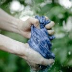 Dłonie wyciskające mokry niebieski materiał na zewnątrz przy roślinach