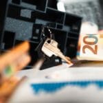 Klucze przy modelu domu na tle euro i wykresów inwestycji