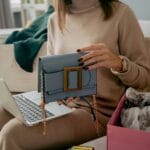 Kobieta na sofie rozpakowuje torebkę kupioną online przy użyciu laptopa