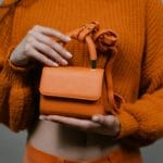 Kobieta trzyma pomarańczową mini torebkę na tle pomarańczowego swetra