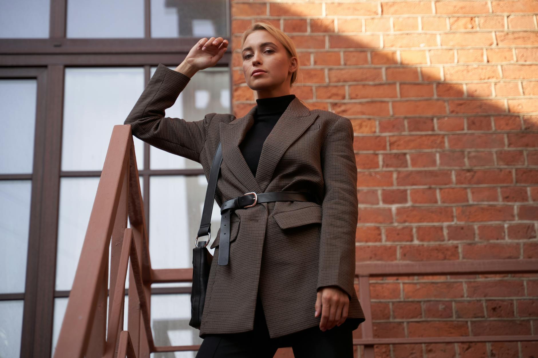 Kobieta w eleganckiej marynarce pozuje na schodach przy ceglanej ścianie