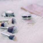 Kosmetyki i pędzle do makijażu ułożone na puszystym białym tle