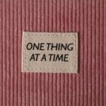 Metka z napisem One Thing at a Time na różowym sztruksie