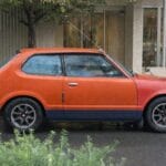 Pomarańczowy klasyczny hatchback zaparkowany na mokrej ulicy w Tokio