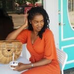 Uśmiechnięta kobieta w pomarańczowej sukience je lody przed kawiarnią