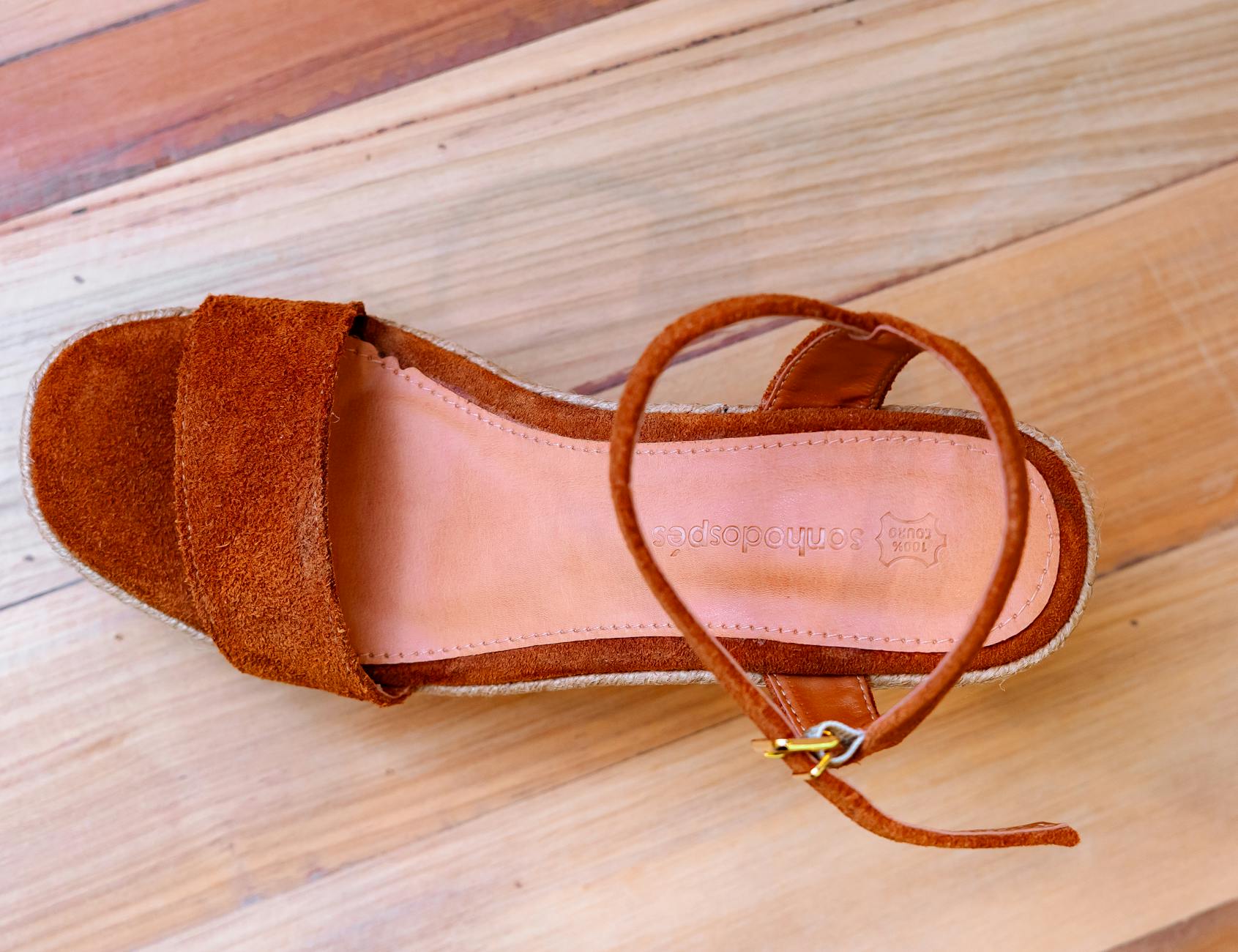 Brązowy sandał z zamszu z paskiem na kostce na drewnianej podłodze