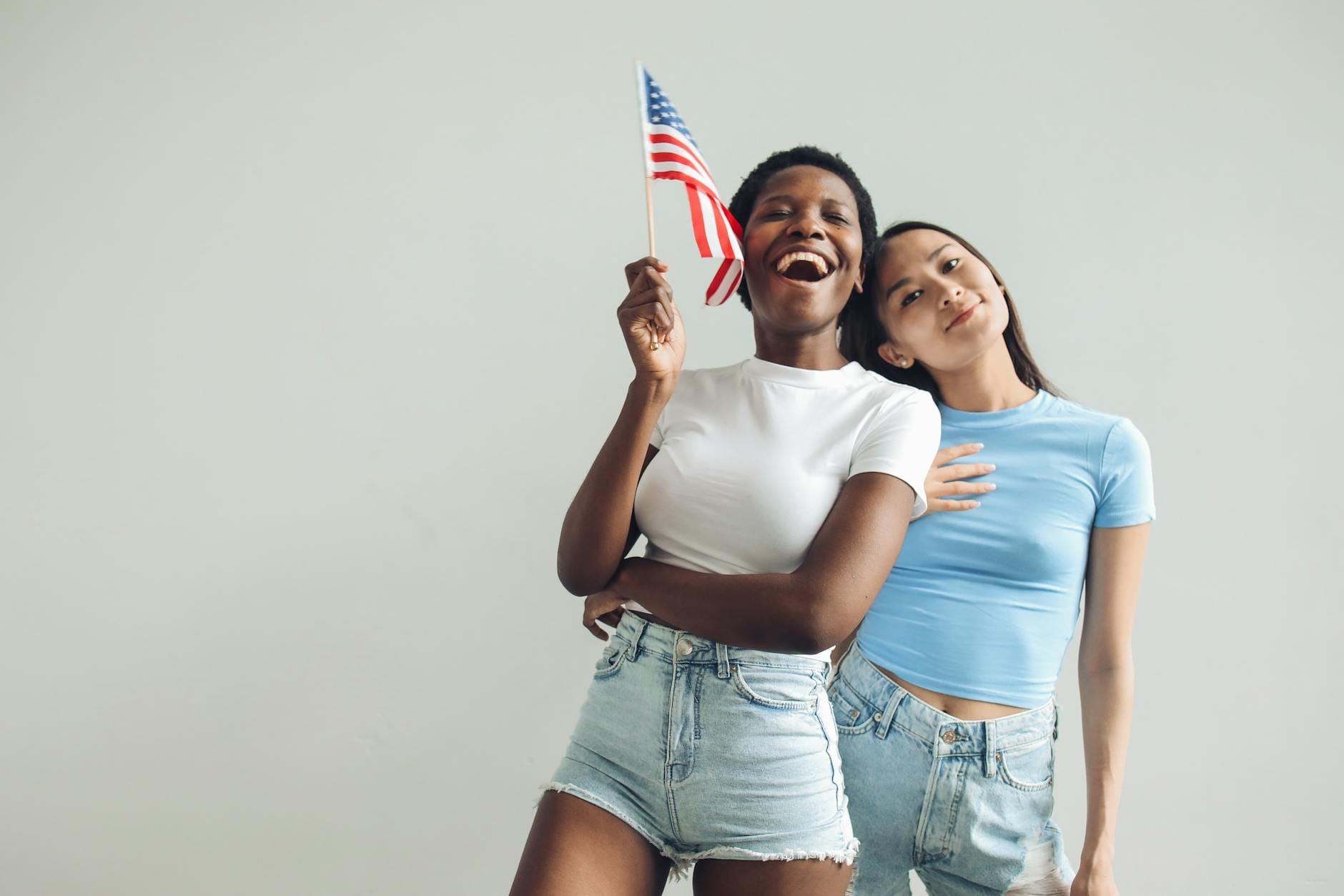 Jak łączyć patriotyzm z codziennym stylem – praktyczny przewodnik po modzie patriotycznej Dwie kobiety w domu radośnie trzymają dużą amerykańską flagę