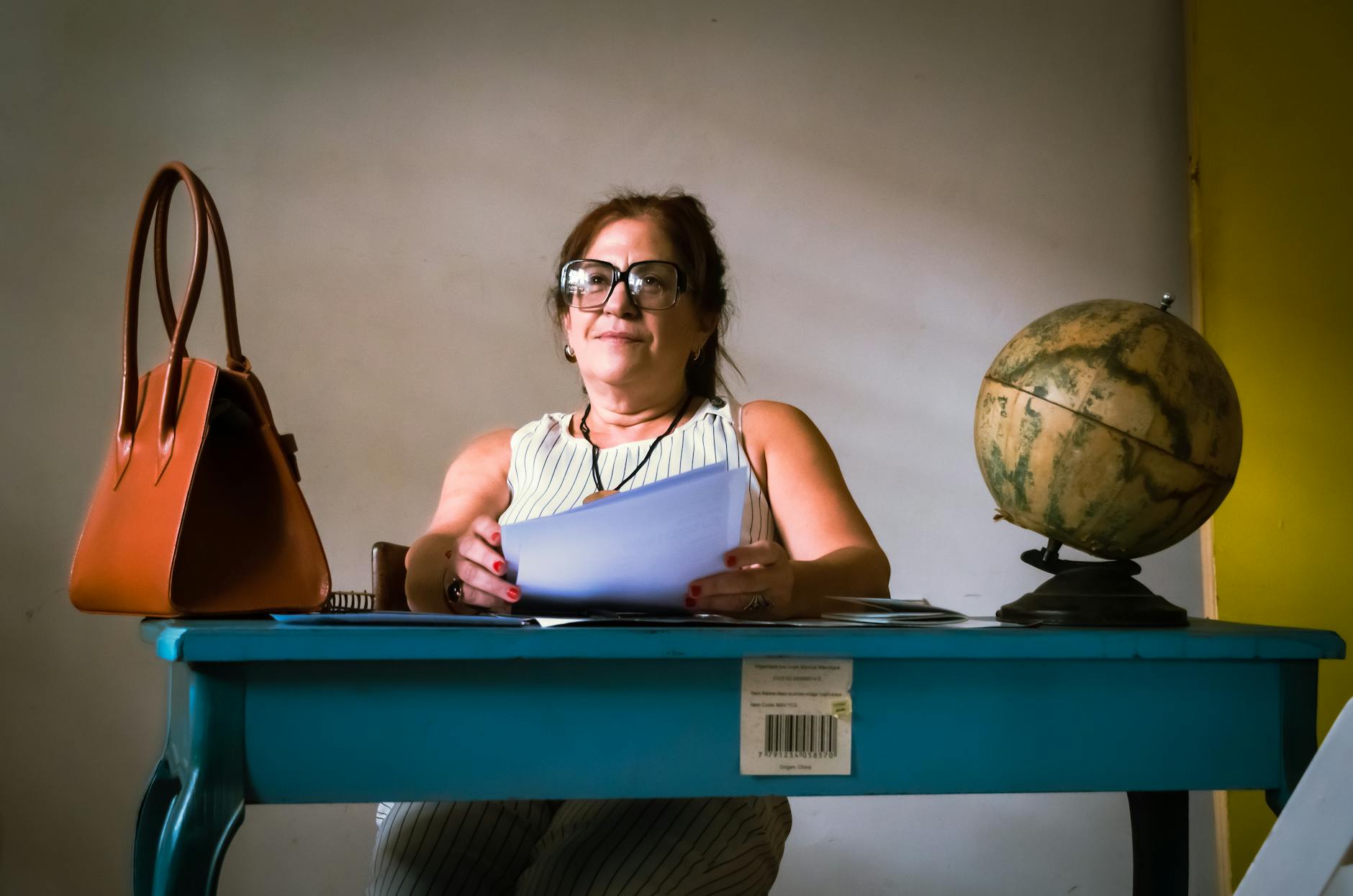 Kobieta przy biurku z torebką, dokumentami i globusem w biurze