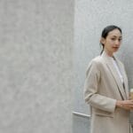 Kobieta w beżowym total looku z kawą na ulicy miasta