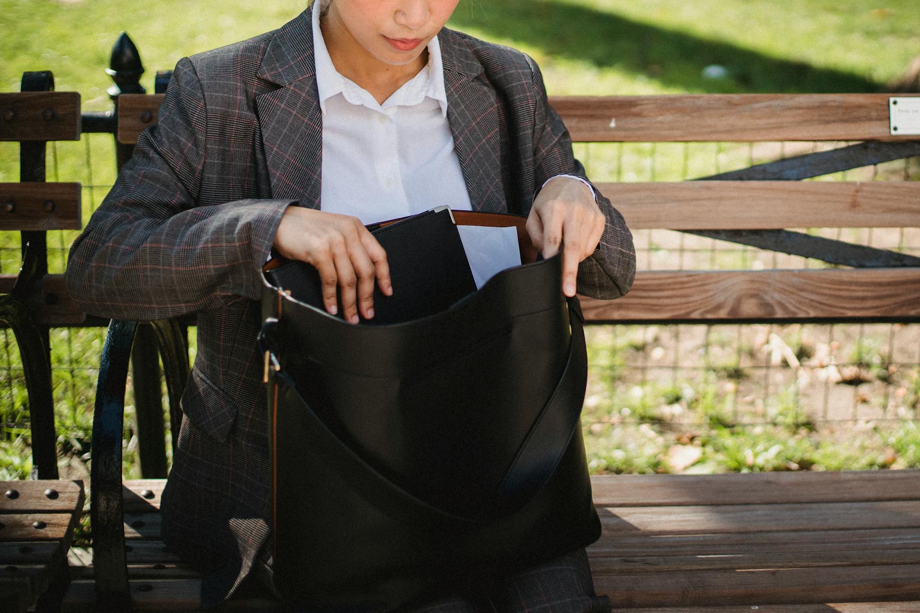 Kobieta w garniturze szuka czegoś w torebce na ławce w parku
