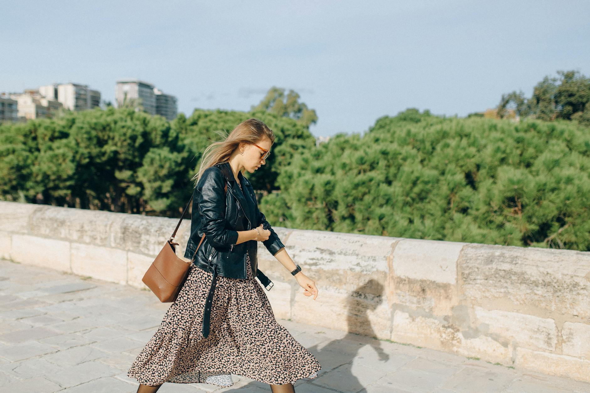 Kobieta w kwiecistej sukience i skórzanej kurtce z torebką na ramię