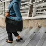 Czarna kobieta w casualowej stylizacji schodzi po schodach z torebką na ramieniu