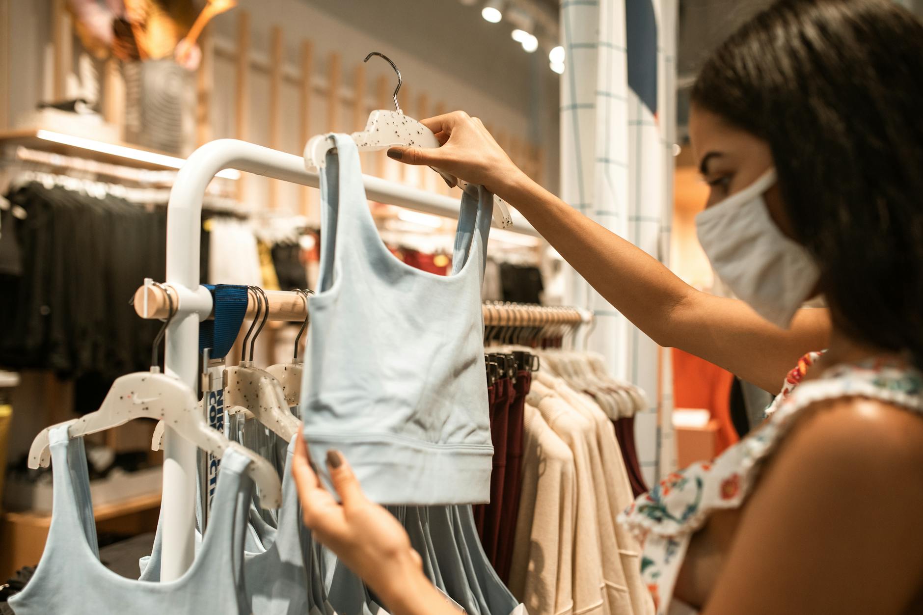 Kobieta w maseczce ogląda sportowe biustonosze w sklepie z odzieżą