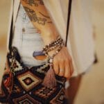 Dłoń z tatuażami trzymająca we wzór torebkę boho z frędzlami