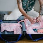 Kobieta klęczy na podłodze i pakuje ubrania do otwartej walizki