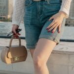 Kobieta na dachu w dżinsowych szortach z torebką i czerwonym manicure