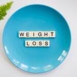 Niebieski talerz z napisem weight loss i liściem paproci na białym tle