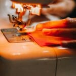 Szycie tkaniny na maszynie z widoczną dłonią prowadzącą materiał