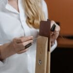Zbliżenie na dłonie szyjące ekoskórę igłą i nicią przy wykańczaniu brzegu